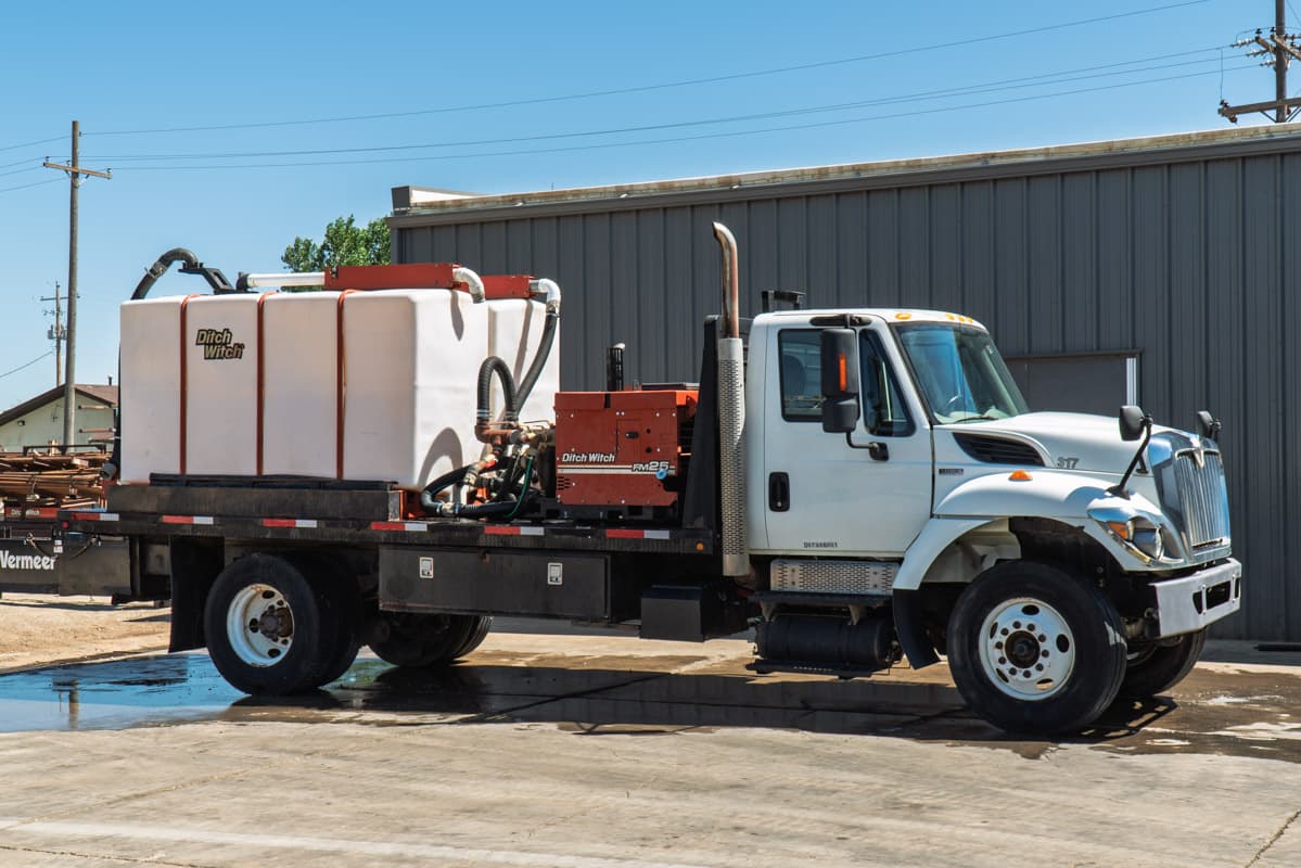 2015 International 7400 mud truck, driver-side view, Ditch Witch FM25 mixer, white poly tank, flatbed, vertical exhaust stack