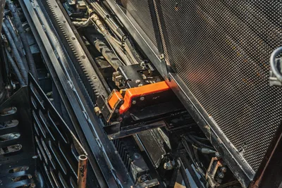 Close-up of Ditch Witch JT24 drill carriage, rack and pinion drive system, hydraulic hoses, and protective mesh guard.