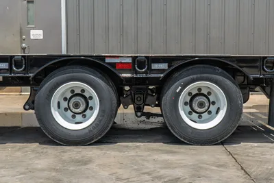 Behnke FB8X30SDPT-40L trailer tandem axle closeup showing Samson dual tires, white steel wheels, black frame, and Behnke badging