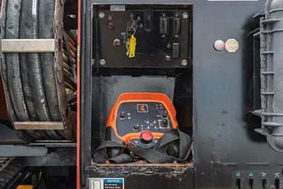 2016 Ditch Witch JT25 operator control panel with ignition, orange remote pendant, e-stop, and fluid hose reel visible at left.
