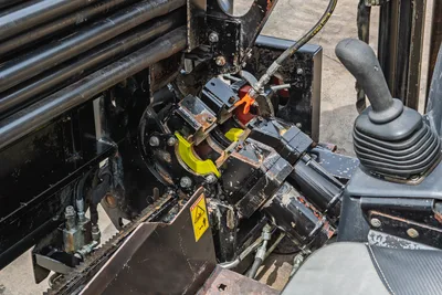 2018 Ditch Witch JT10 spindle/carriage close-up showing pipe rack, vise jaws, hydraulic lines, and operator joystick control