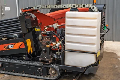 2018 Ditch Witch JT10 HDD drill showing side-mounted fluid tank, drill pipe rack, rubber tracks, and exposed hydraulic lines.