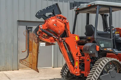 2024 Ditch Witch RT125Q Quad with vibratory plow attachment extended, orange hydraulic arm, rubber tracks, ROPS cab visible