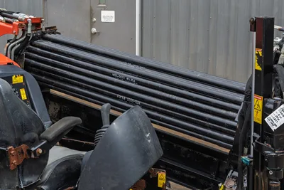 Ditch Witch JT10 drill pipe rack and operator station showing pipe stack, hydraulic controls, and warning labels.