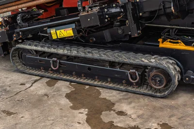 2016 Ditch Witch JT25 rubber track close-up showing tread, drive sprocket, tie-down hooks, and hydraulic components above
