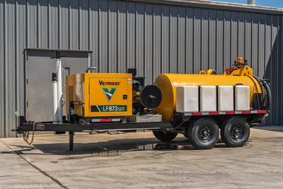 Vermeer LP873SDT trailer-mounted vacuum excavator, driver-side view, yellow debris tank, white poly water tanks, spoil hose, tandem axle