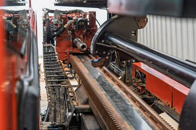 Close-up side view of Ditch Witch JT3020 drill rack, carriage, hydraulic hoses, and rack-and-pinion drive mechanism.