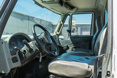 2015 International 7400 mud truck cab interior showing steering wheel, instrument cluster, manual shifter, and worn driver seat