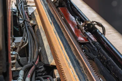 2017 Ditch Witch JT20 drill frame rack-and-pinion thrust system, close-up showing wear-used rack teeth, hydraulic hoses, and fittings