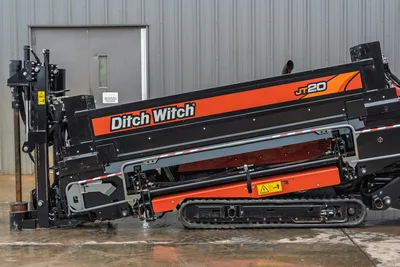 Ditch Witch JT20 HDD unit side view with orange and black boom, tracked undercarriage, drill head assembly, and hydraulic controls visible
