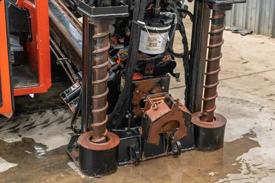 Close-up of Ditch Witch JT3020 drill head, carriage, rusted anchor assembly, and hydraulic lines on HDD drill rig.