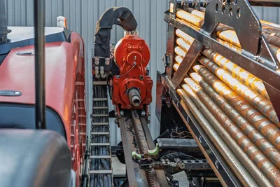 2021 Ditch Witch JT28 red spindle drive head on drill frame with rack gear, hydraulic hoses, and loaded 10ft drill pipe rack visible
