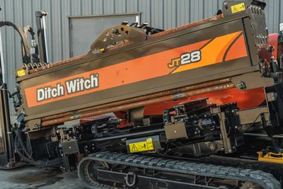 2021 Ditch Witch JT28 HDD drill close-up, angled drill frame with loaded pipe rack, rubber tracks, hydraulic components visible