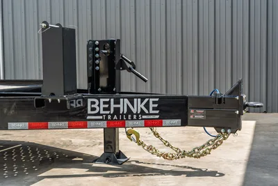 Behnke CBCT2324E-BT-R trailer tongue close-up showing adjustable coupler, drop-leg jack, safety chains, and diamond-plate fenders