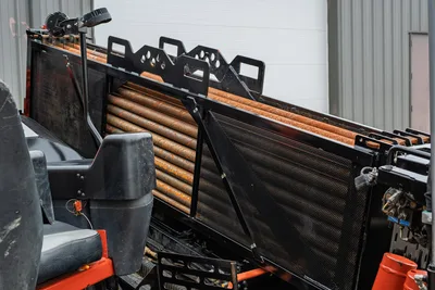 Ditch Witch JT24 drill pipe rack loaded with used 2.25" HDD drill stems, mesh side guards, operator seat visible left