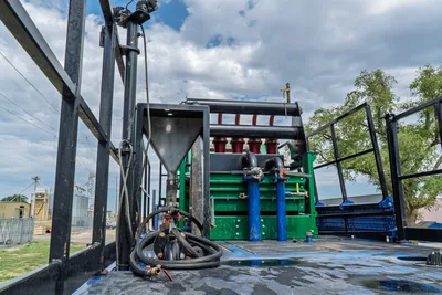 American Augers M300DH mud recycler deck showing hopper, desander cones, shaker screens, blue standpipes, and coiled suction hoses