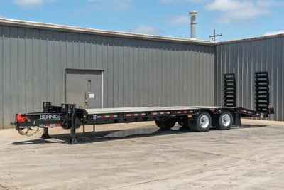 2026 Behnke FB8X30SDPT-40L flatbed trailer, driver-side angle, wood deck, dual tandem axles, fold-down ramps, front jacks, red coiled airlines