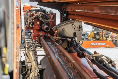 Close-up side view of 2023 Ditch Witch JT20 drill carriage, rack and pinion drive, hydraulic lines, and drill pipe rack.
