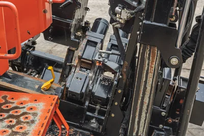 Close-up of Ditch Witch JT25 pipe loading system, showing drill rod carriage, vises, and drill string alignment mechanism.