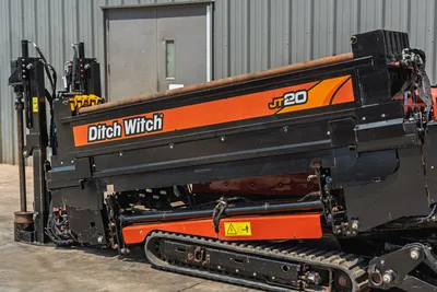 2021 Ditch Witch JT20 HDD drill, side view showing drill frame, rubber tracks, pipe rack with drill pipe, and hydraulic vise components.