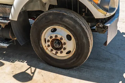 2015 International 7400 HDD mud truck front steer tire, 11R22.5, rusty white steel wheel, worn tread, mud flap visible