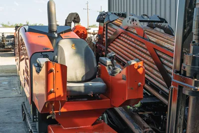 2021 Ditch Witch JT28 operator seat, joystick controls, exhaust stack, and loaded drill pipe rack viewed from rear-side angle