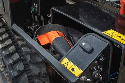 Ditch Witch JT24 operator storage compartment open, showing orange locating receiver, safety harness, warning decals, and control switches nearby.