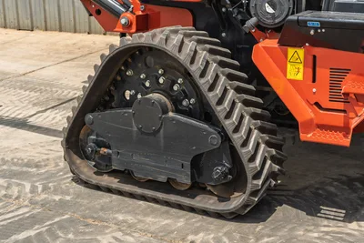 2024 Ditch Witch RT125Q rubber track close-up, drive sprocket, undercarriage rollers, orange frame, caution decals visible