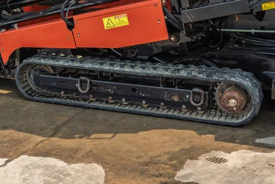 2017 Ditch Witch JT30 rubber track close-up showing drive sprocket, track frame, tie-down loops, and orange chassis with danger decal