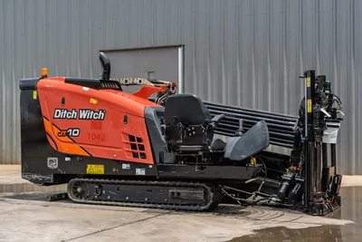 2018 Ditch Witch JT10 HDD drill rig, side view, orange cab, rubber tracks, loaded drill pipe rack, carriage assembly visible