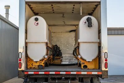 Rear view of 2000 Freightliner FL80 mud truck showcasing dual poly tanks and drilling fluid pump system mounted in box.