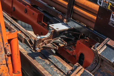 2014 Ditch Witch JT100 Mach 1 drill frame closeup showing pipe vise, rack-and-pinion carriage, wear on components, stacked drill pipe in background