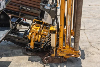 Vermeer D24x40 S3 drill carriage, vise assembly, and thrust frame close-up with loaded drill pipe rack, worn paint, hydraulic hoses visible