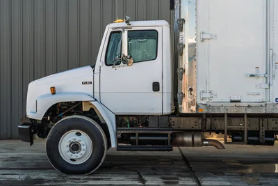 Side profile of 2000 Freightliner FL80 mud truck with white cab, box body, and exposed engine compartment components.