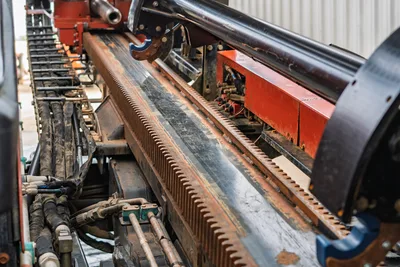 Ditch Witch JT3020 Mach 1 drill rack and drive assembly with visible gear track, hydraulic lines, and carriage mechanism.