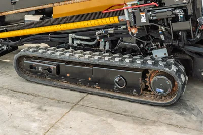 2024 Vermeer D20x22 S3 rubber track undercarriage close-up showing drive sprocket, hydraulic lines, and yellow drill pipe rack