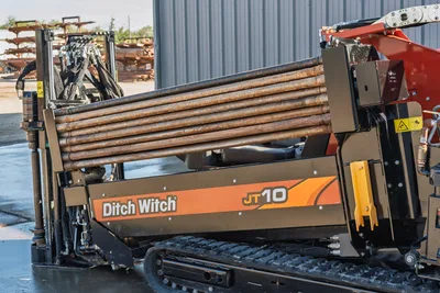 Ditch Witch JT10 HDD rig loaded with drill pipe, side view showing 9,000 lbs thrust capacity and red rotary head assembly
