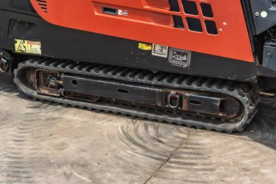 2017 Ditch Witch JT20 rubber track close-up, worn undercarriage with tie-down hook, safety decals visible on red frame