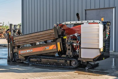 Ditch Witch JT10 HDD unit with tracked undercarriage, drill pipe rack, red boom arm, and white mud tank assembly, side profile view