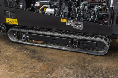 Ditch Witch JT20 engine compartment and rubber tracks, side view showing hydraulic systems and warning labels