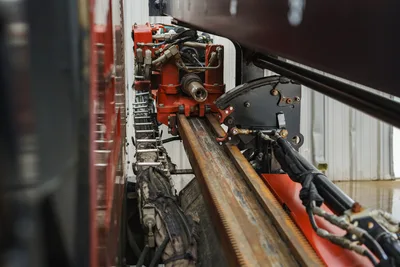 2015 Ditch Witch JT20 drill frame close-up showing rack-and-pinion carriage, red spindle drive, hydraulic lines, and wear-used thrust rail.