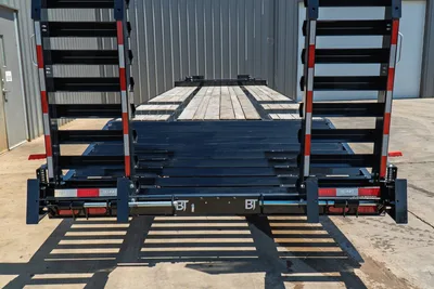 Behnke FB8X30SDPT-40L trailer rear view showing folded steel ramps, wood deck, spring-assist hinges, and BT-branded rear bumper with reflectors.