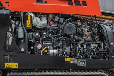 Ditch Witch JT20 engine compartment showing 74 hp diesel engine, hydraulic pump, cooling system, and electrical components with safety labels