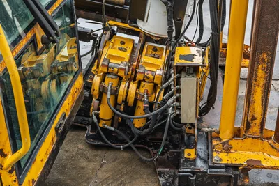 Close-up of Vermeer 40x55 S3 hydraulic vise assembly, including control valve, hydraulic lines, and operator cab frame.