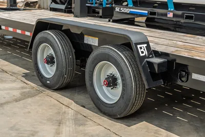 Behnke CBCT2324E-BT-R trailer tandem axle closeup showing dual tires, white steel wheels, red hub caps, black fenders with BT logo