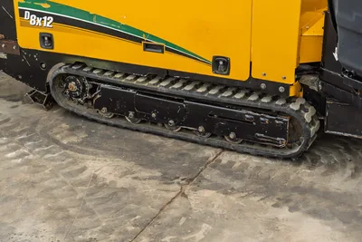 2018 Vermeer D8x12 HDD drill close-up of rubber track undercarriage showing drive sprocket, rollers, and worn yellow chassis panel.