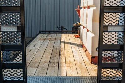 2023 MAXX-D C6X trailer deck view showing wood plank flooring, expanded metal side rails, diamond plate ramp, and white poly mud tanks with red frame.