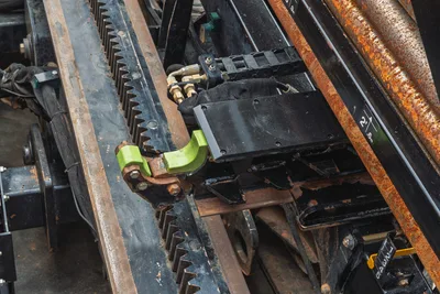 Close-up of Ditch Witch JT25 rack and pinion carriage, drill pipe racking system, and hydraulic hoses on drill frame.