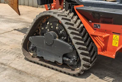 2024 Ditch Witch RT125Q rubber track close-up showing drive sprocket, roller frame, and chevron tread pattern; minimal wear