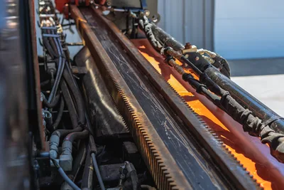 Close-up of rack-and-pinion drill frame gear teeth and hydraulic hose routing on a 2021 Ditch Witch JT20 HDD drill rig.